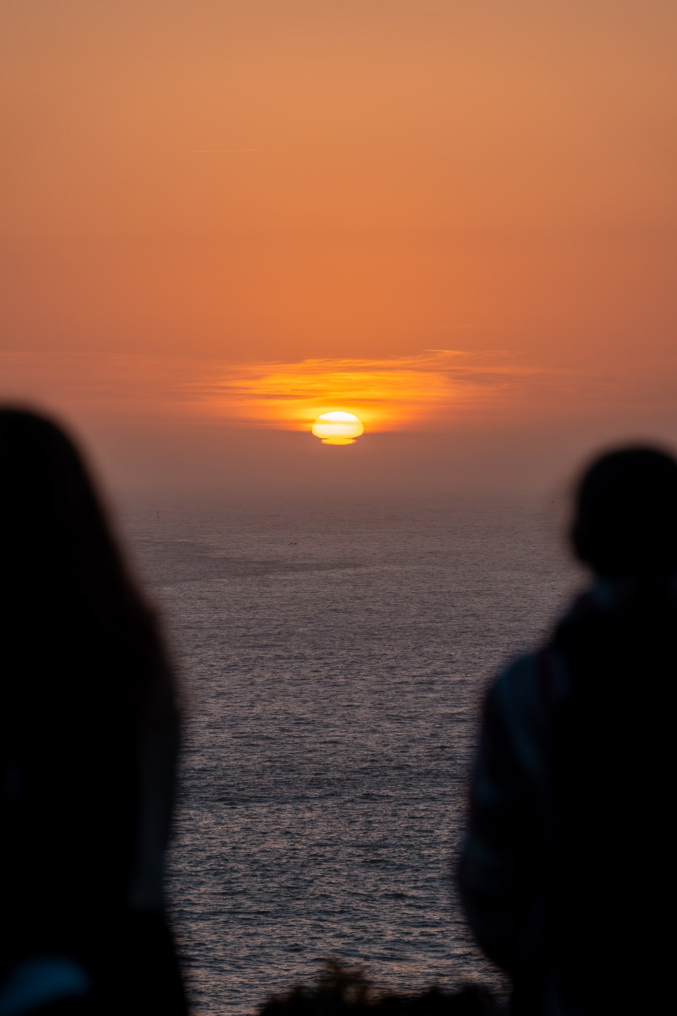 Silhouettes of two people framed by a vibrant sunset sky, creating a warm and intimate scene