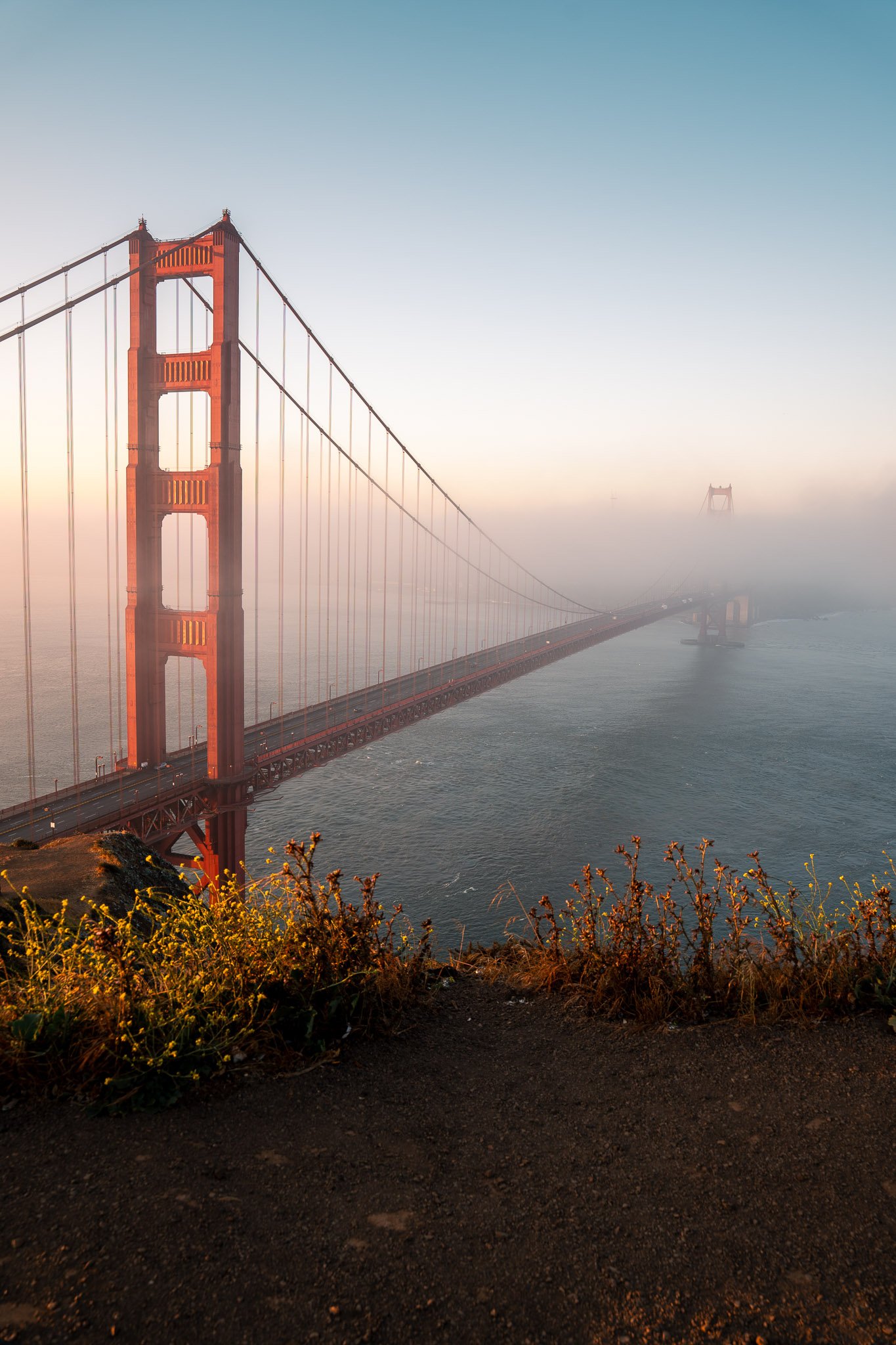 Vertical view of the Golden Gate Bridge at sunrise with golden light casting over San Francisco Bay