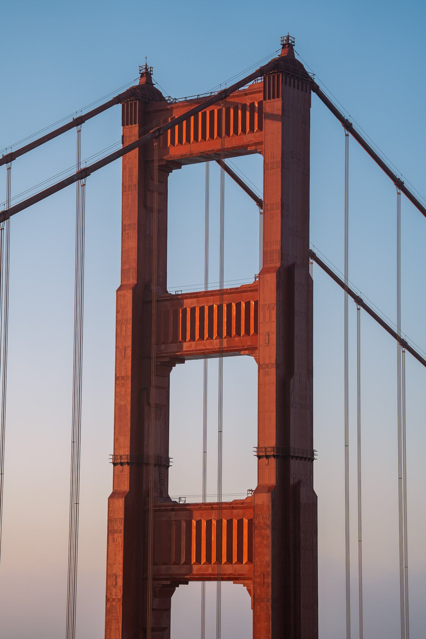 Close-up view of a Golden Gate Bridge tower glowing warmly in the soft light of sunrise