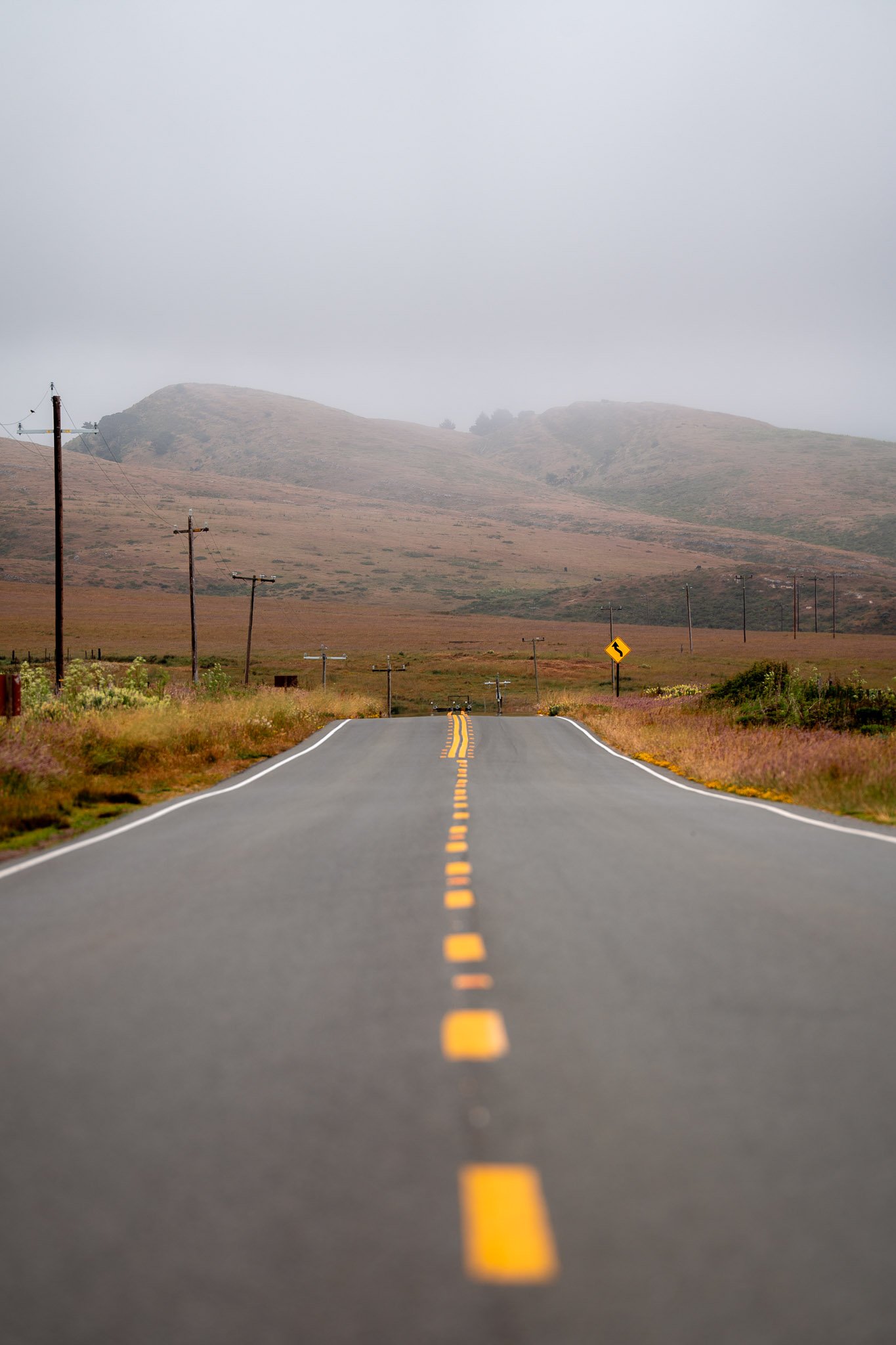 Long, flat road vanishing into a white foggy horizon with minimal surroundings