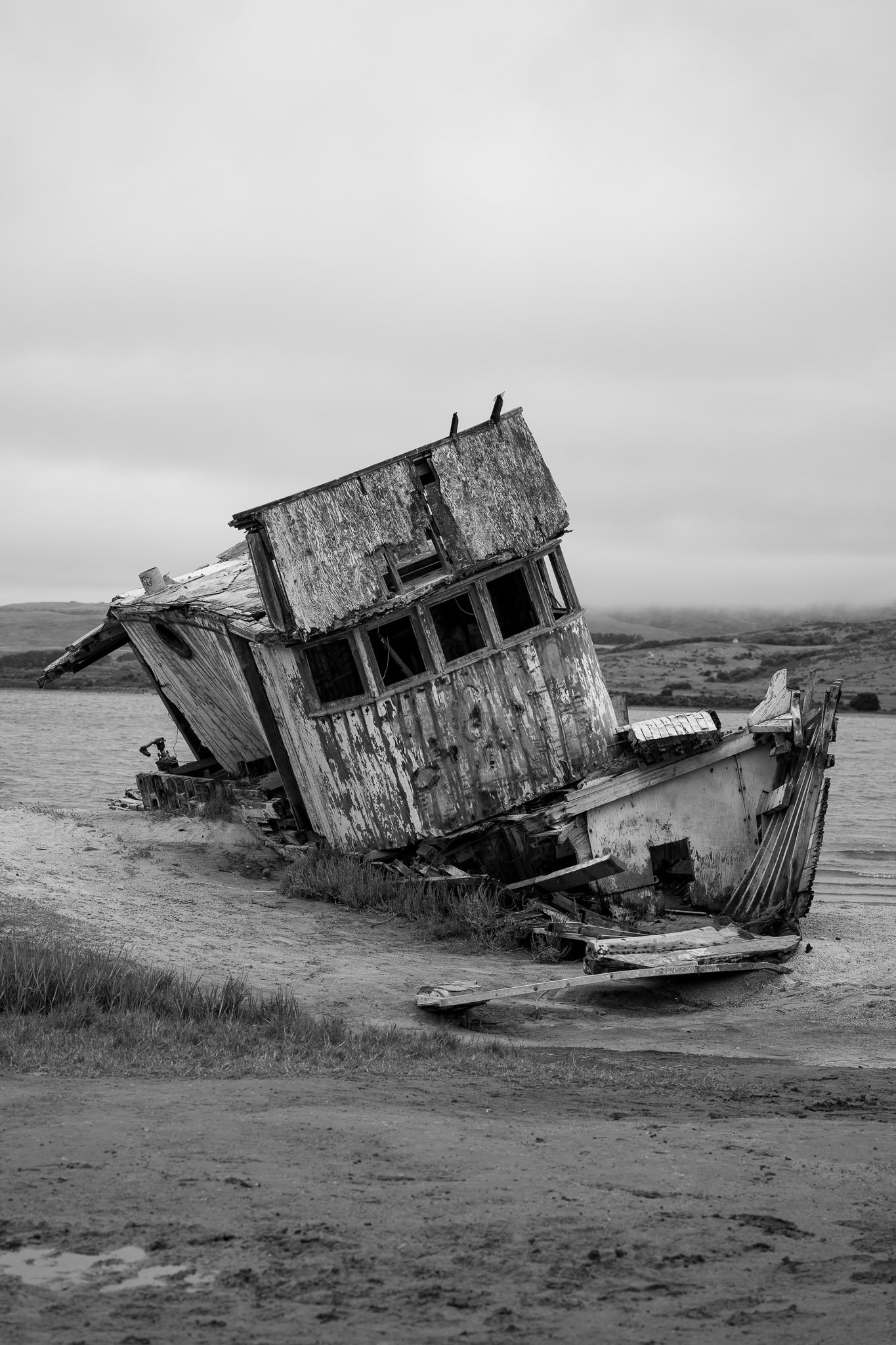 Black and white image of an abandoned shipwreck resting on a rocky shoreline, evoking a haunting atmosphere
