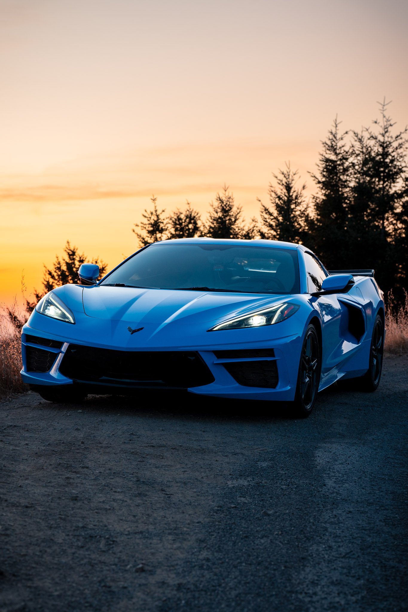 Sleek blue Corvette sports car parked with a vibrant sunset sky in the background